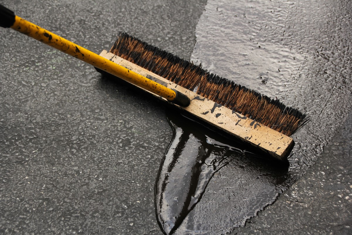 A close up of a large sweeper-style broom spreading the best driveway sealer option