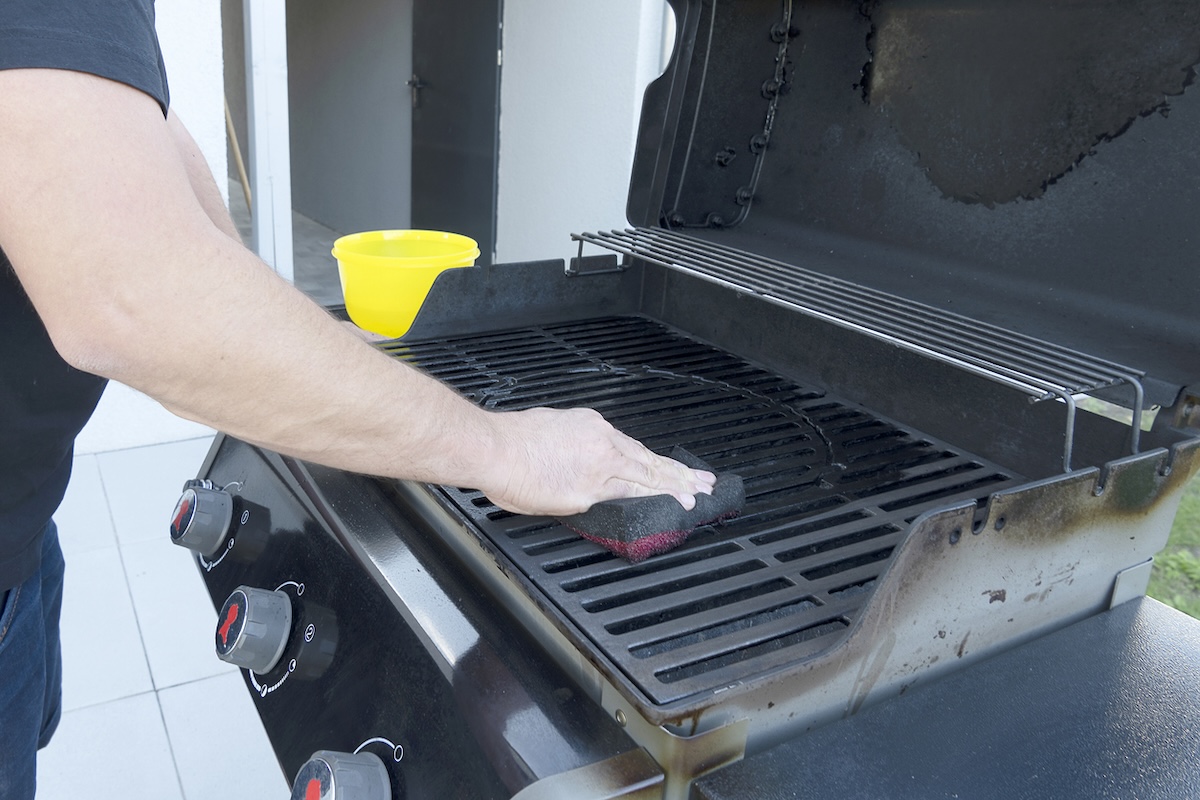 Man using sponge to clean grill cooktop.