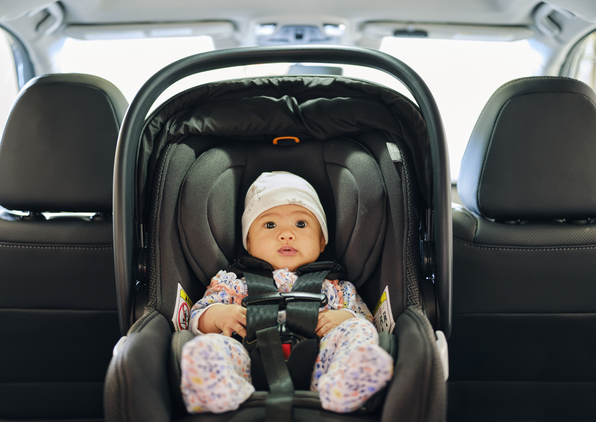 A 3 month old baby sitting in a carseat in the backseat of an auto.