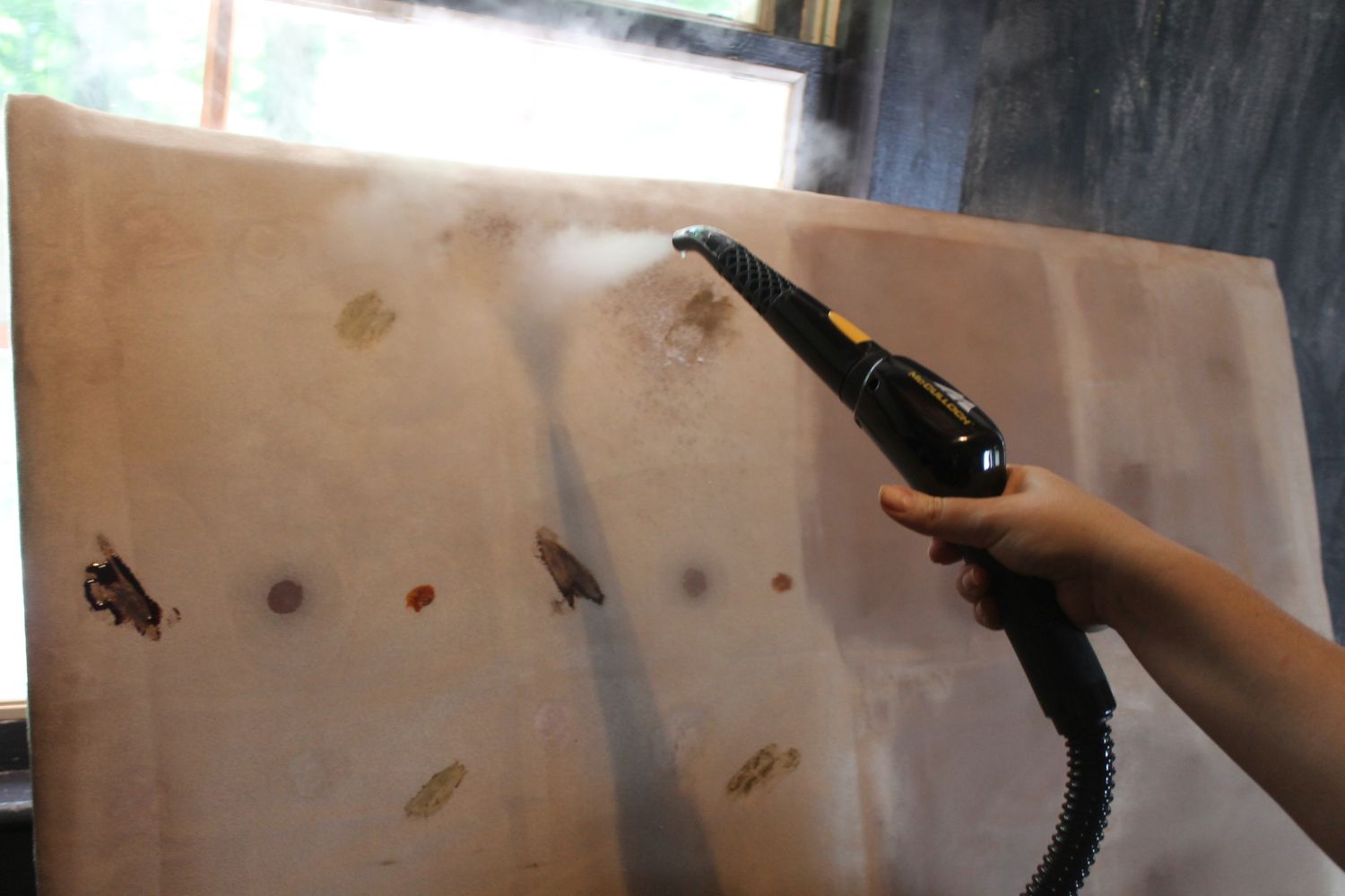 A person using the best handheld steam cleaner to remove many different types of stains