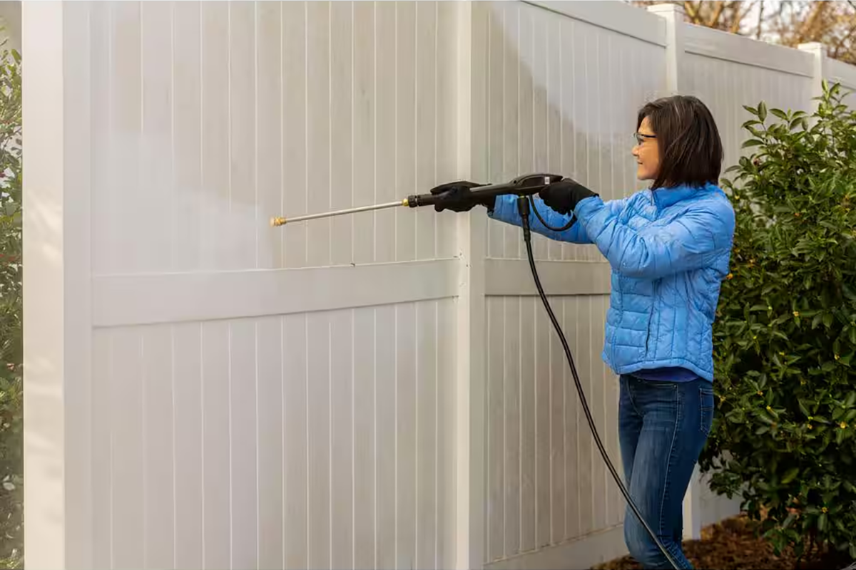 A person pressure washing a white fence using Ecolab Exterior House & Siding  Concentrate from The Home Depot.