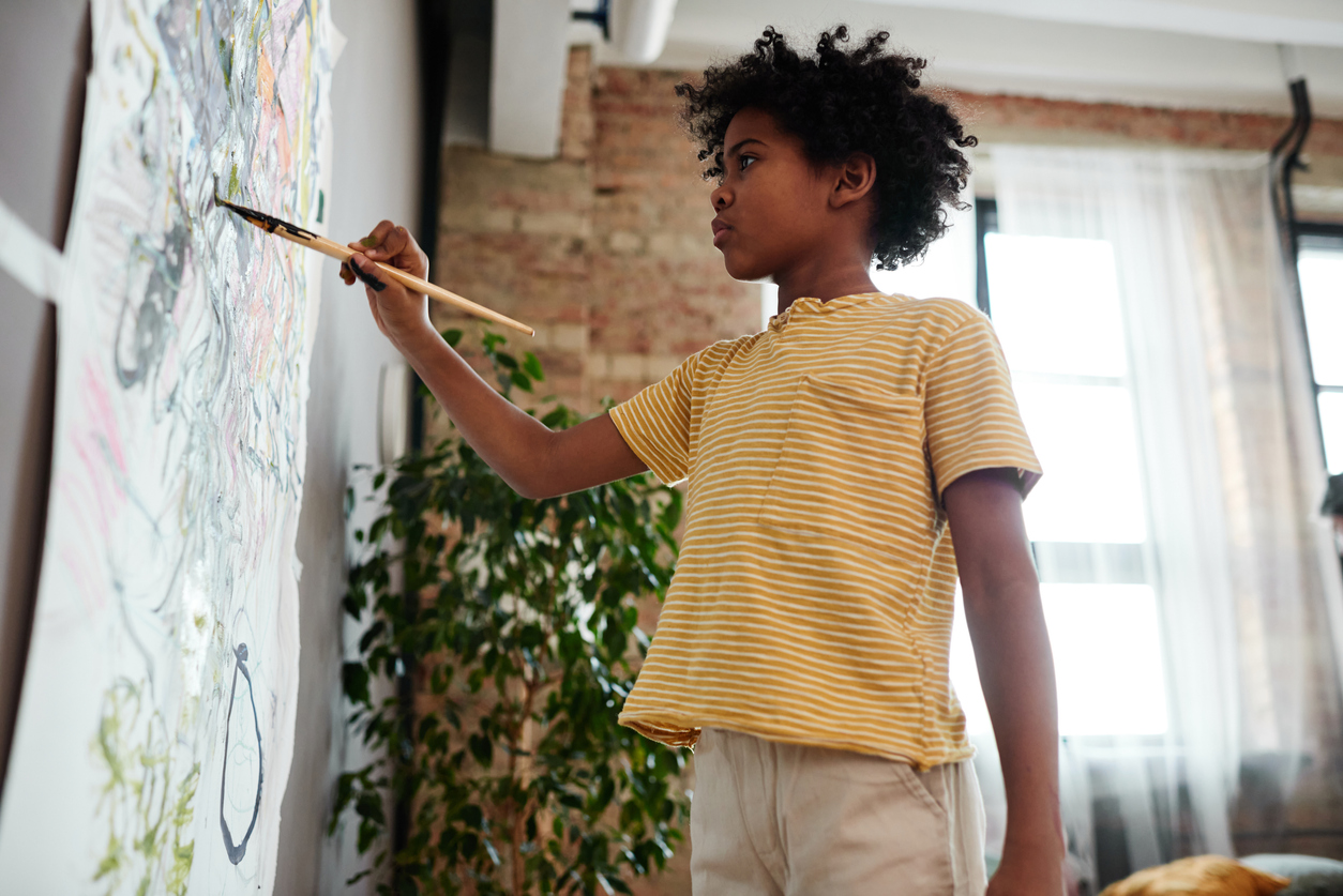 child in striped shirt painting on paper taped to wall