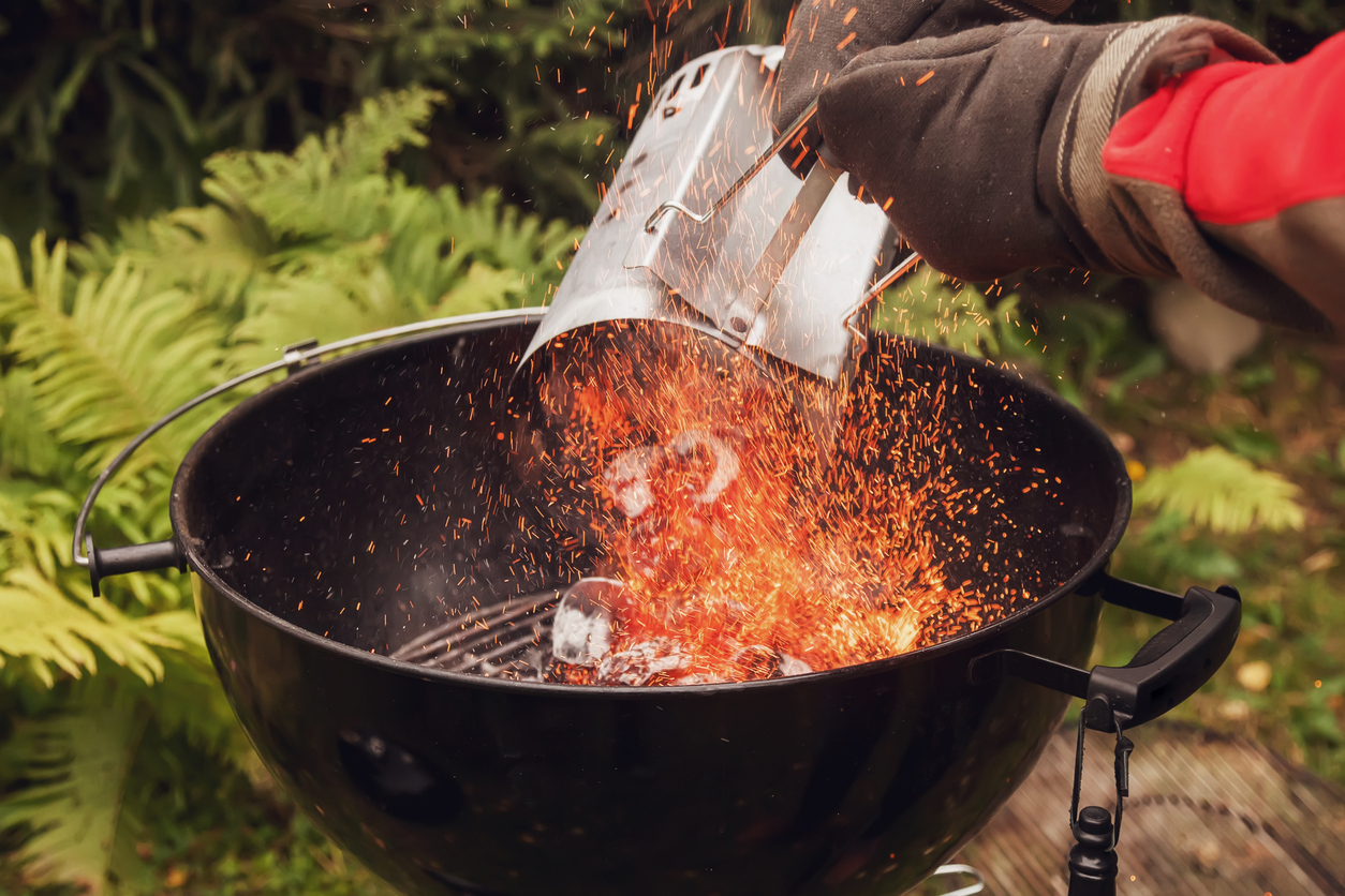 Person pours hot coals from a charcoal chimney onto a charcoal grill.