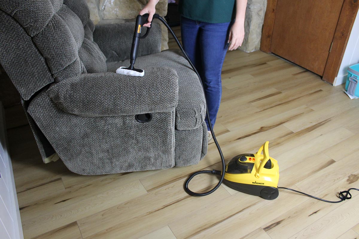 Woman steam cleaning the arm of a gray recliner