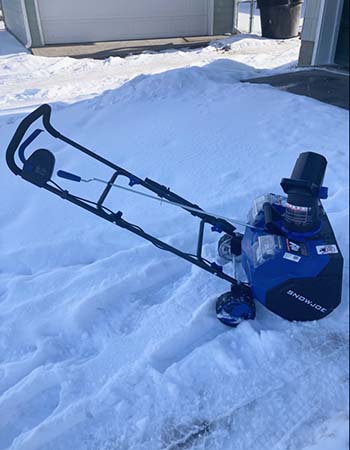 The Snow Joe Single-Stage Snow Blower on a snowy surface with several tracks around it during testing.