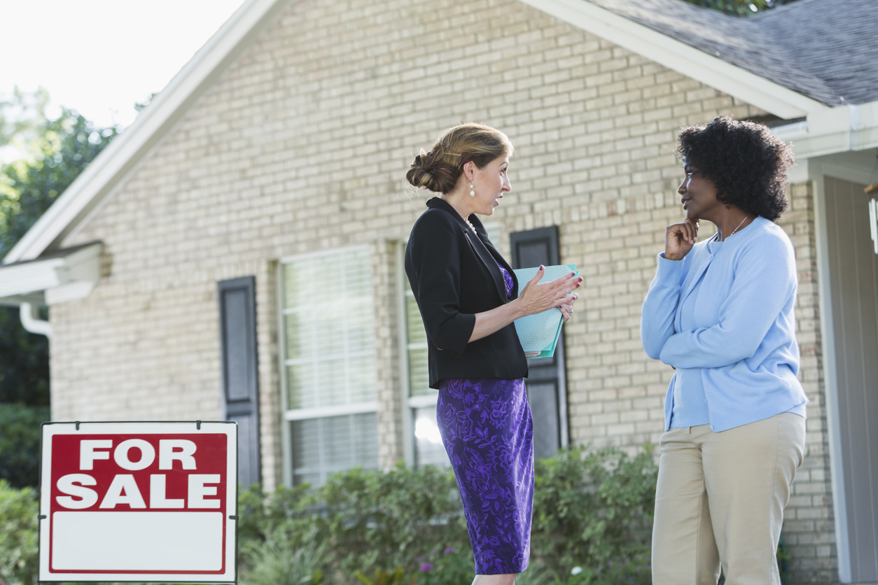 iStock-509182770 hériter d'une maison agent immobilier parlant à une femme à l'extérieur d'une maison avec un panneau à vendre