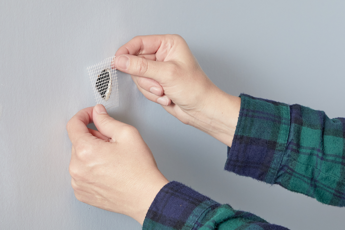 Woman covers a hole in drywall with drywall mesh tape.