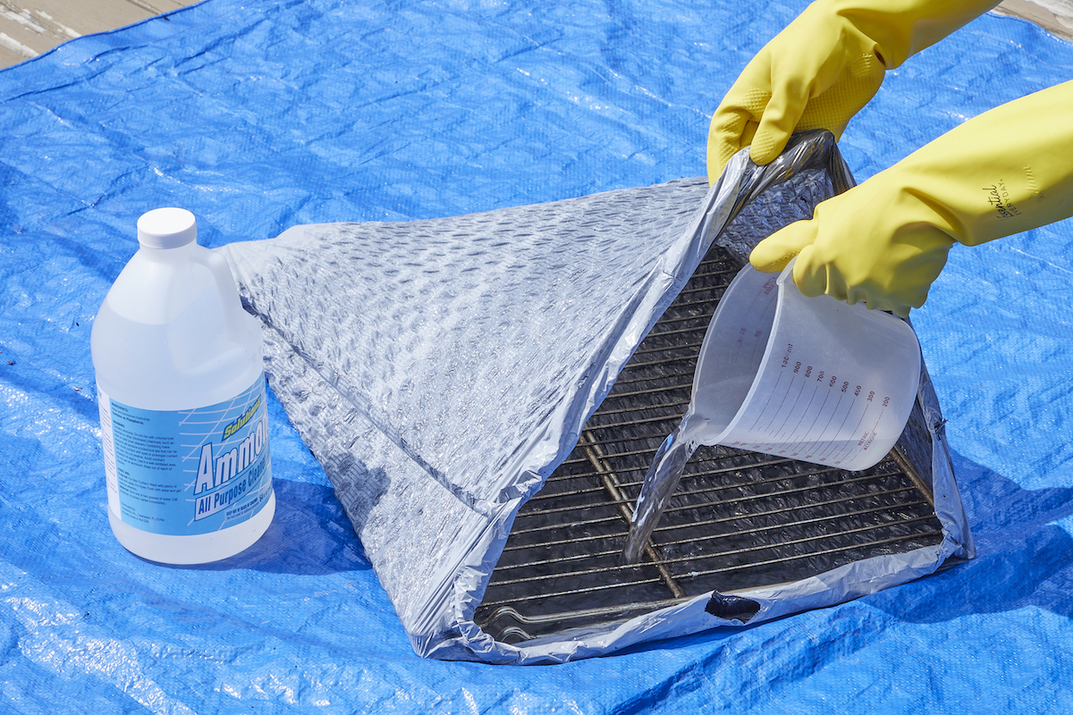 Woman adds ammonia to a trash bag with oven racks inside.