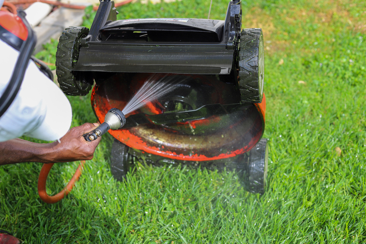 Man sprays deck of lawn mower with a garden hose to clean it.