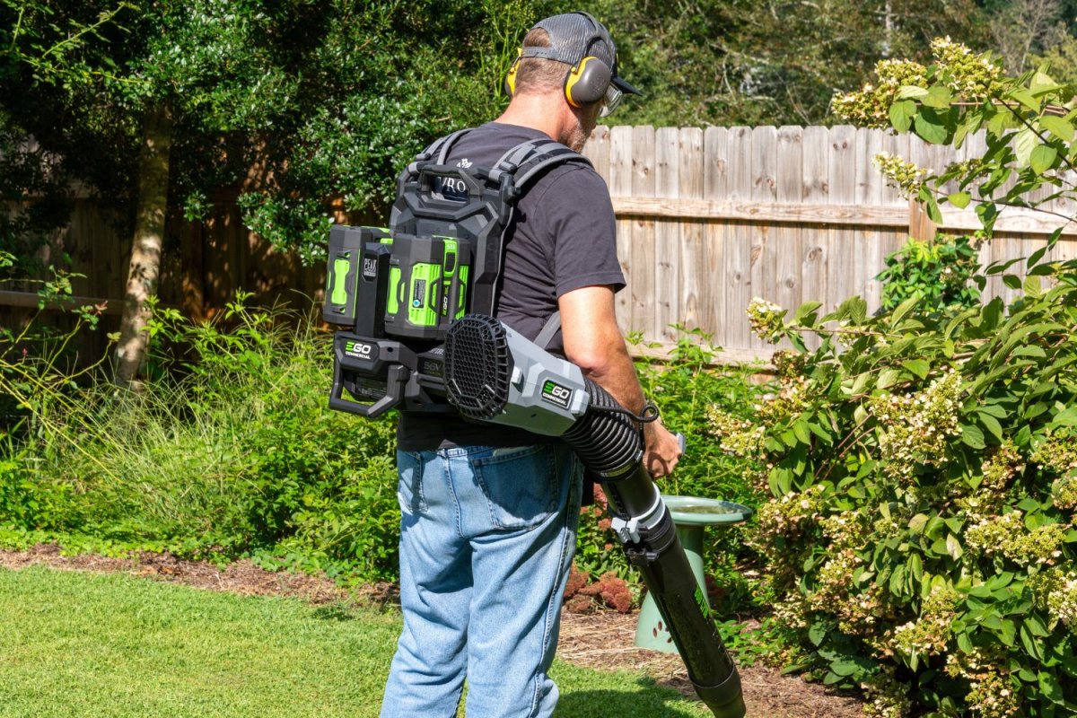 Une personne portant la meilleure option de souffleur de feuilles à dos et des protections auditives pendant qu'elle nettoie le périmètre de son jardin.