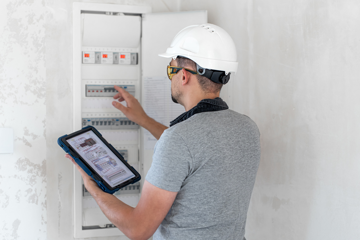 Un inspecteur de l'énergie examine le tableau électrique d'une maison avec un casque de sécurité.