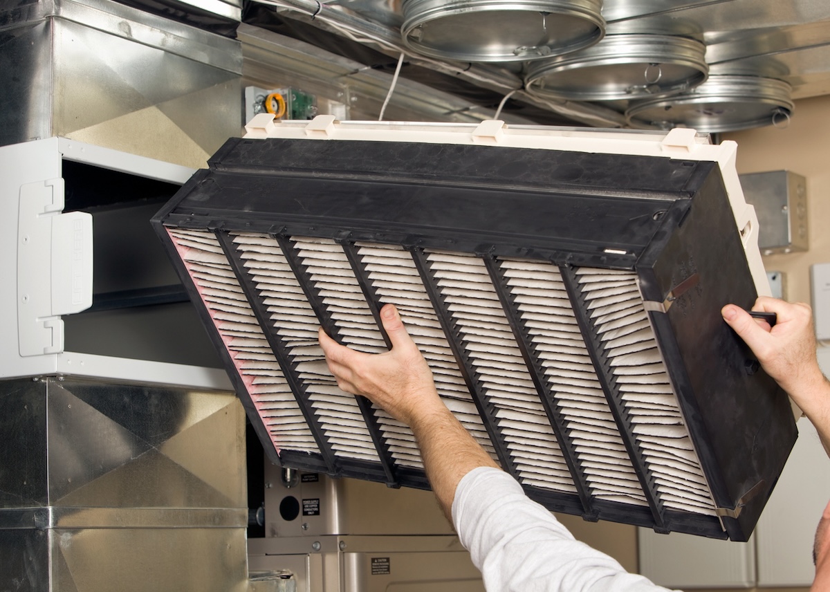 A person replacing the filter on a whole-house air cleaner air purifier installed in a residential home.