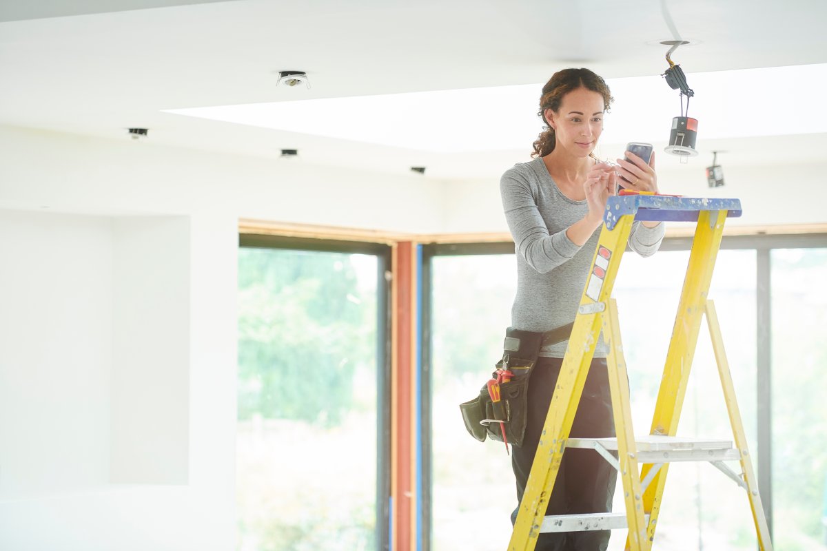 Electrician on a yellow ladder fixes a lighting issue in a home.