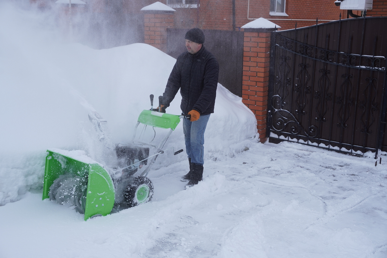 Un homme nettoie la neige en hiver dans la cour de la maison, un homme nettoie la neige avec une souffleuse à neige