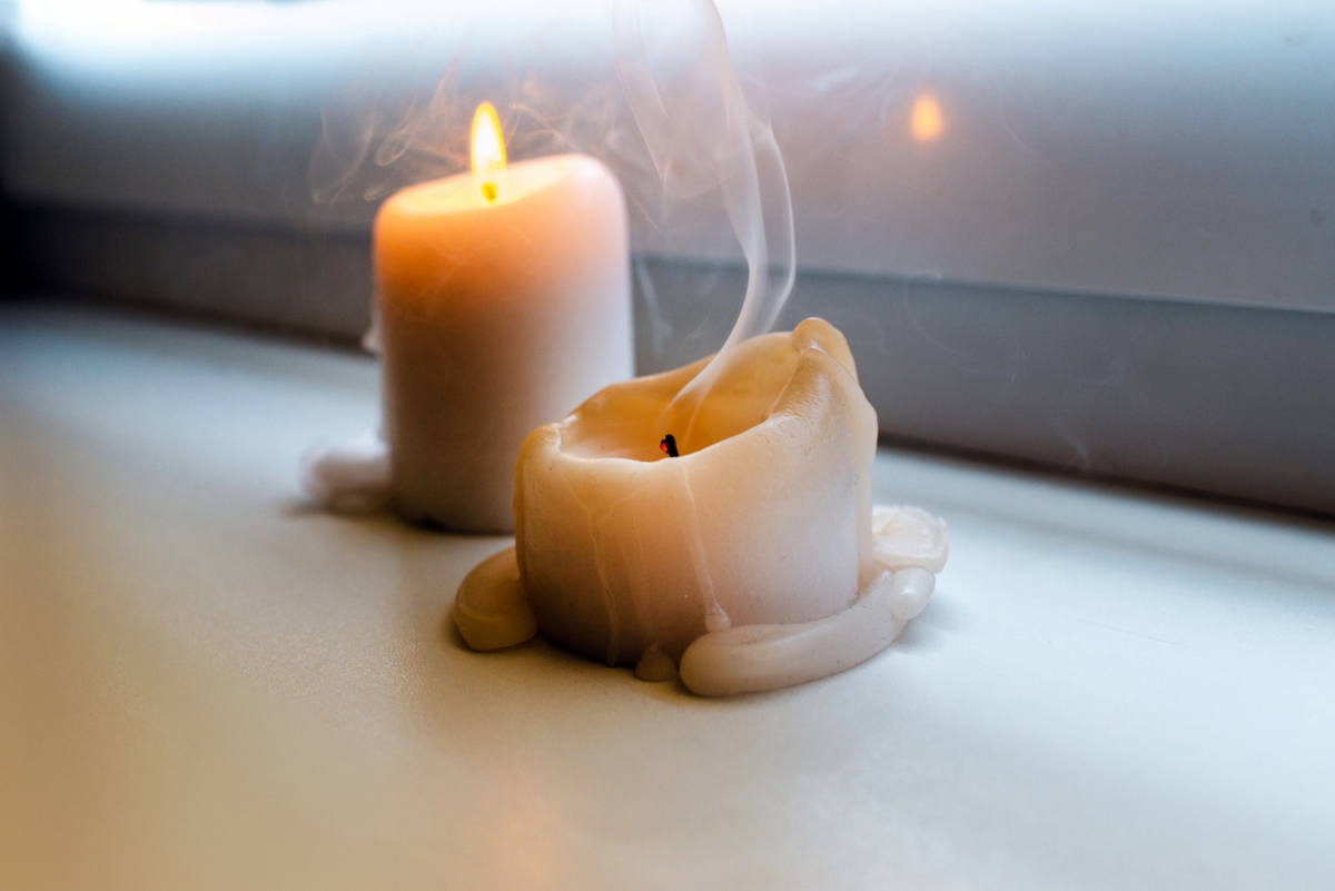 Two candles by windowsill and one blown out.