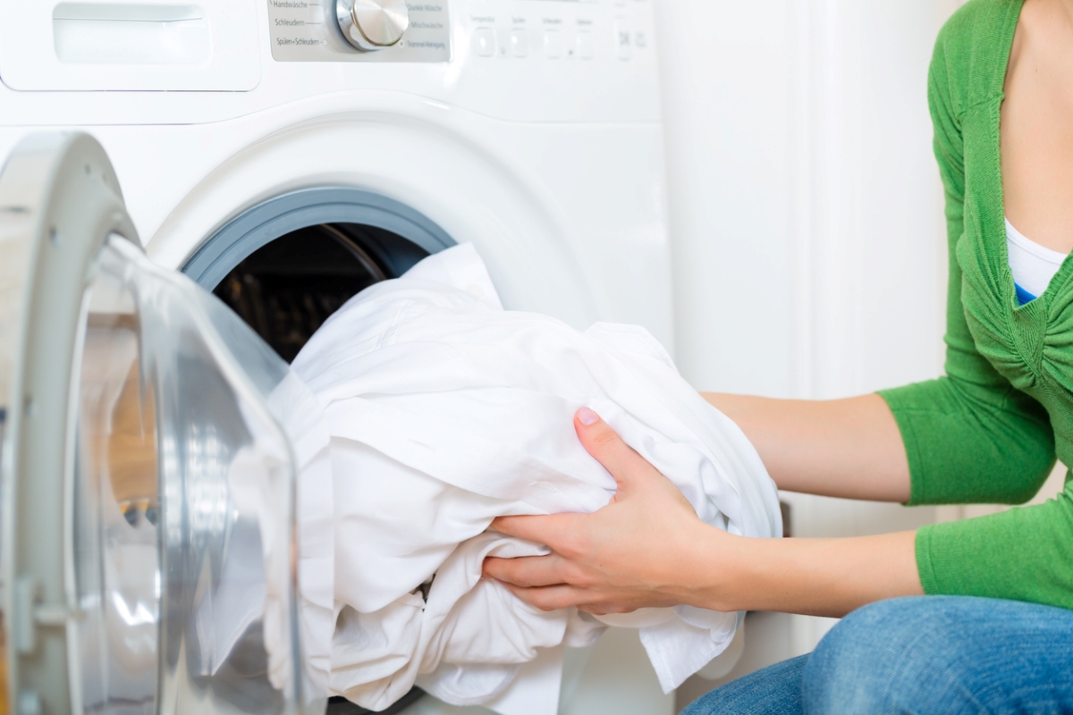 Person putting white bed sheets in dryer.