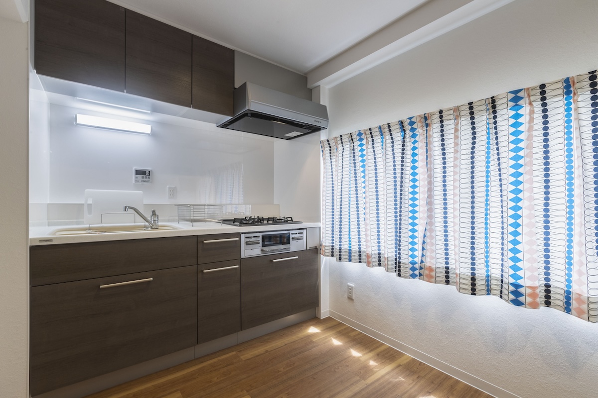 A small kitchen with a large window covered by a patterned curtain.