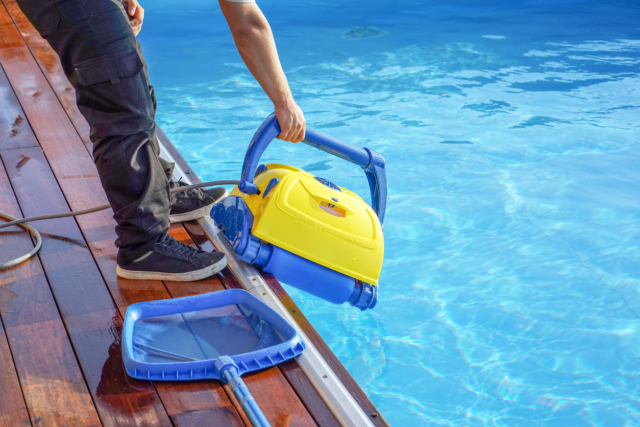 A worker places a pool vacuum into a pool to clean it.