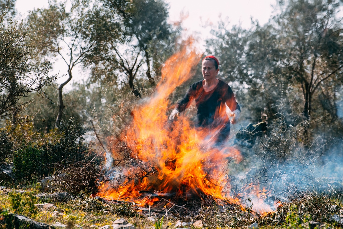 A woman in a red bandana tends to a burning pile of yard waste.