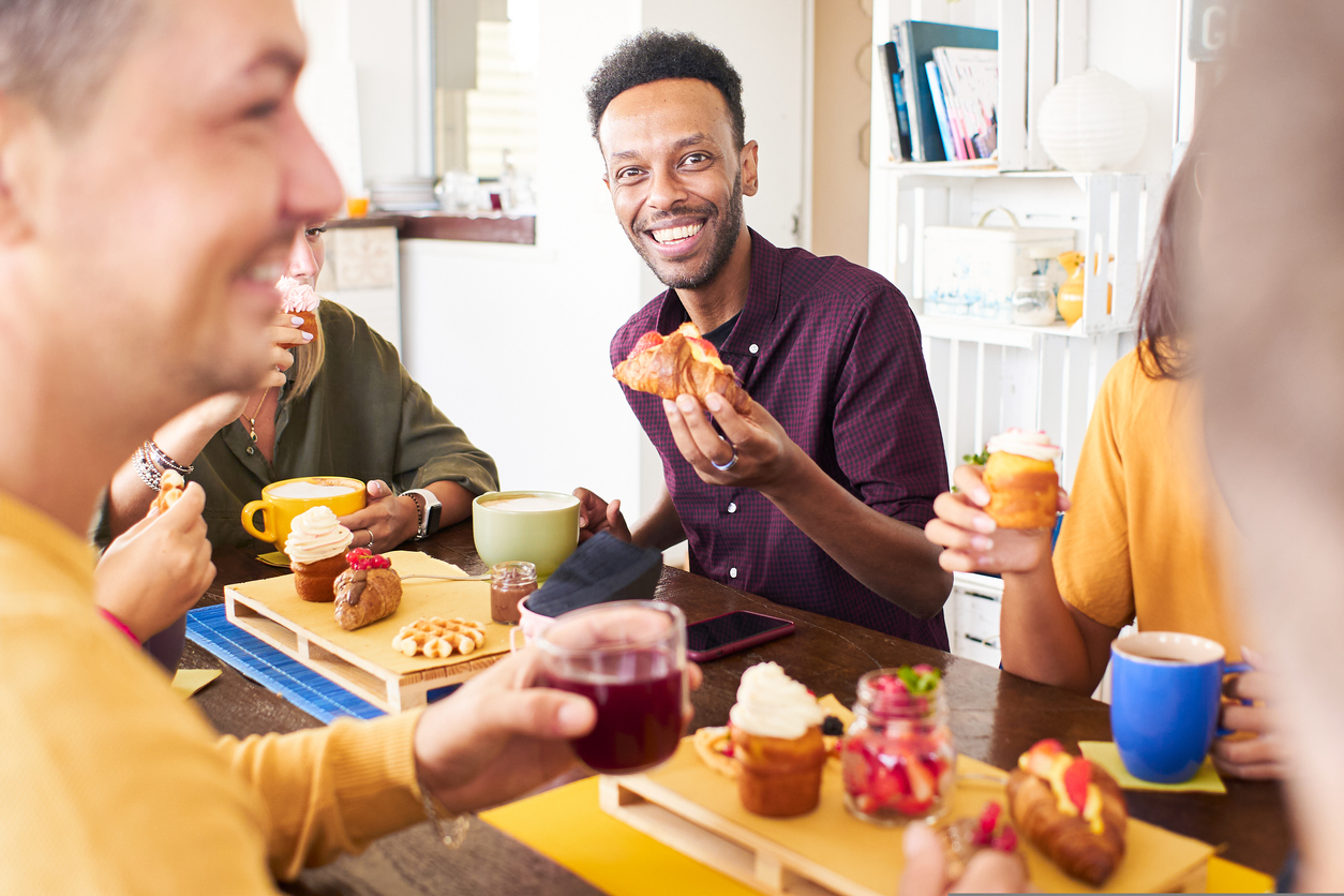 Friends taking breakfast time drinking juices coffee and eating cakes. People having fun at cafeteria. Lifestyle and community concept with happy men and women at cafe bar. High quality photo