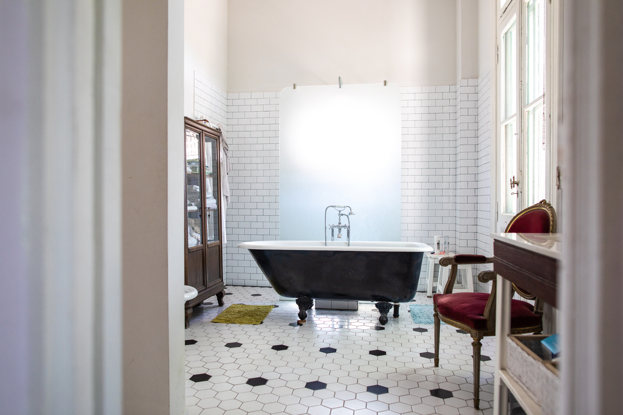 Une baignoire autoportante noire se trouve dans une salle de bain vintage noire et blanche avec des meubles anciens.