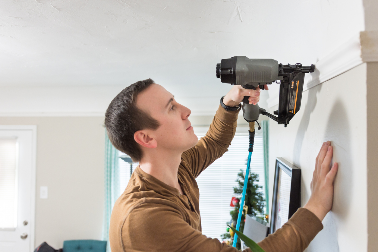 Young man uses nail gun to install crown molding in home.