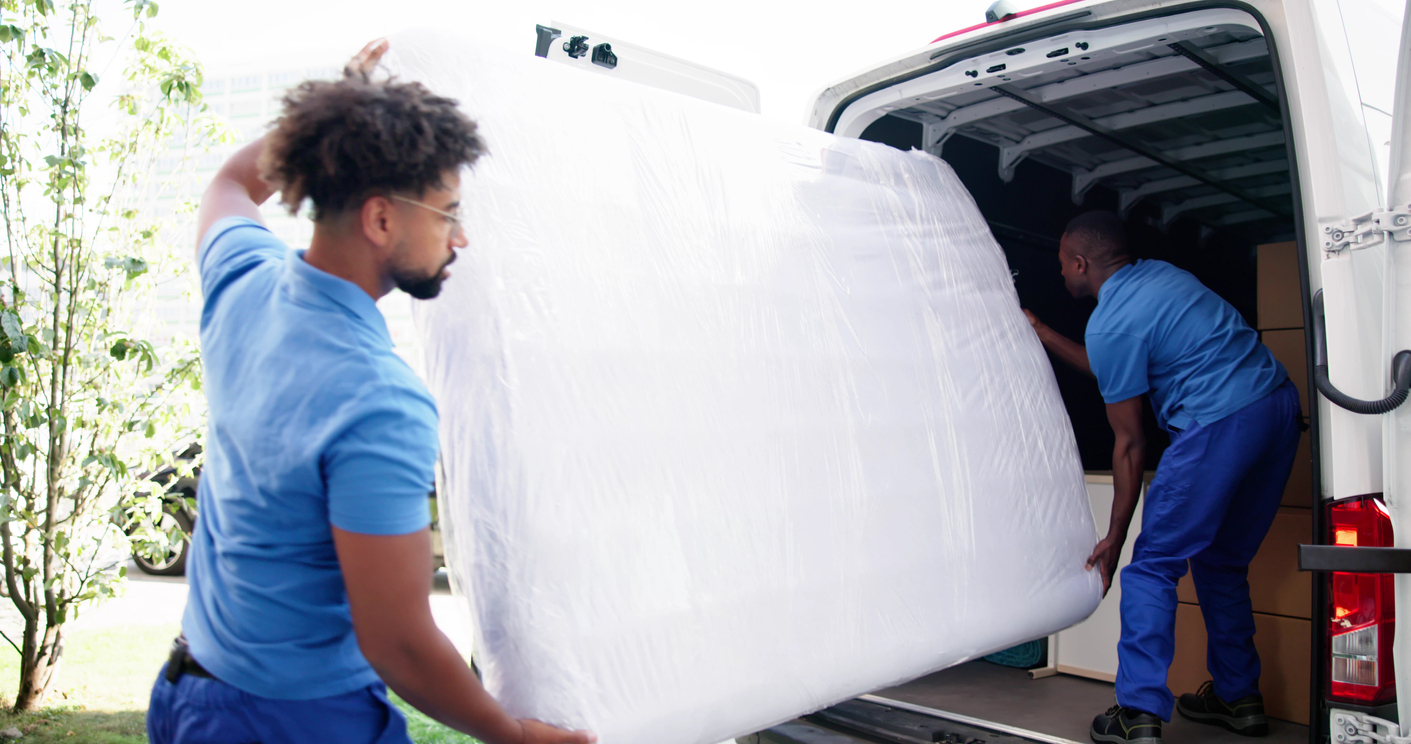 Deux hommes chargent un matelas à l’arrière d’une camionnette.