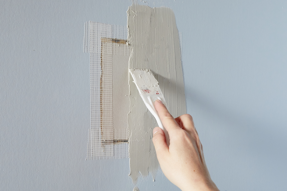 Using joint compound to cover a patched hole in drywall.