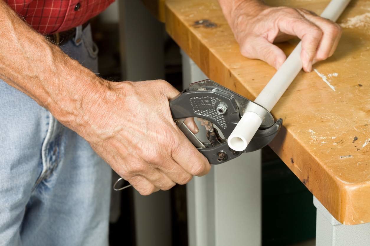 Man cuts a PVC pipe using a pipe cutter.