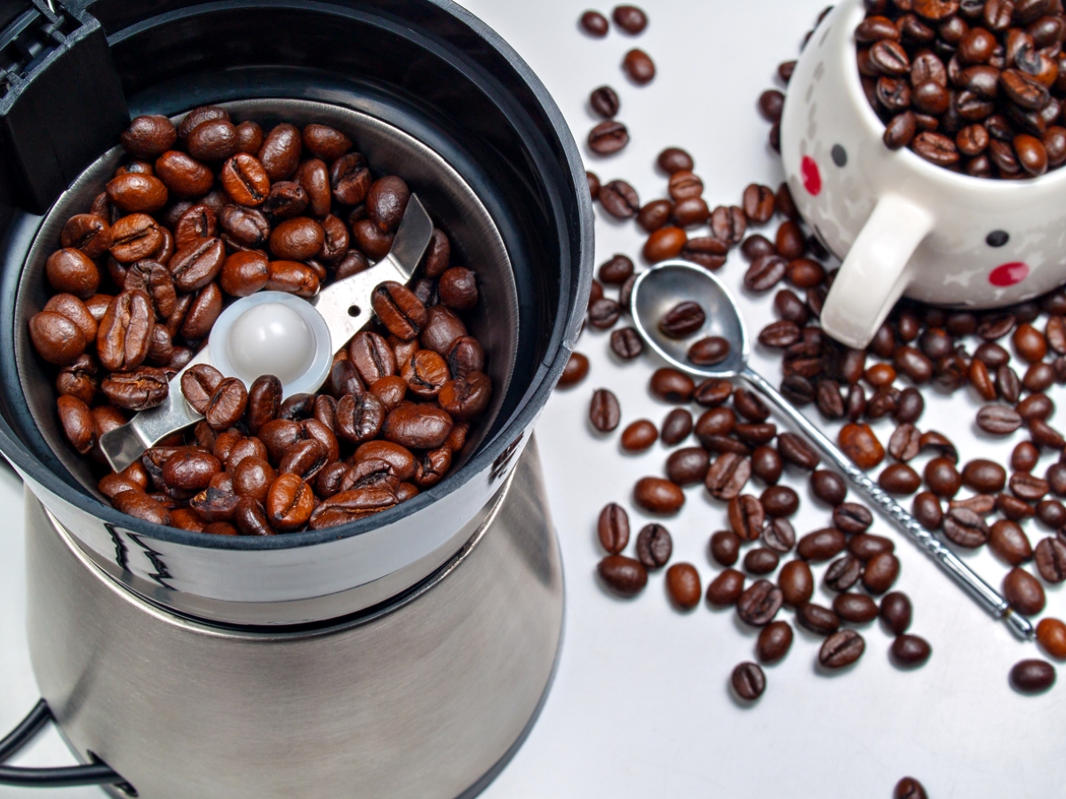 Coffee beans in coffee grinder and on table.