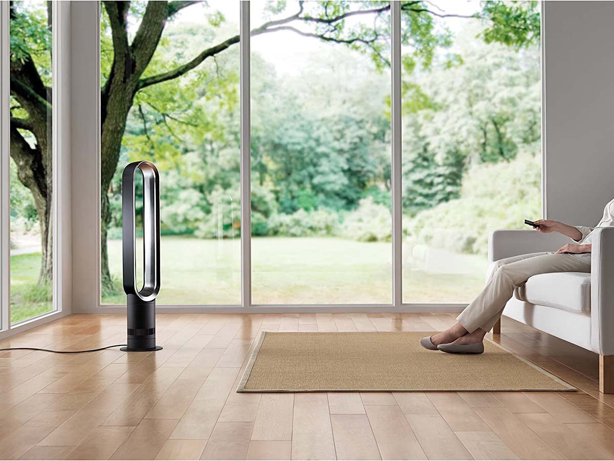 A dyson fan in a spacious sunroom with large windows in the background that look out at a spacious yard and trees