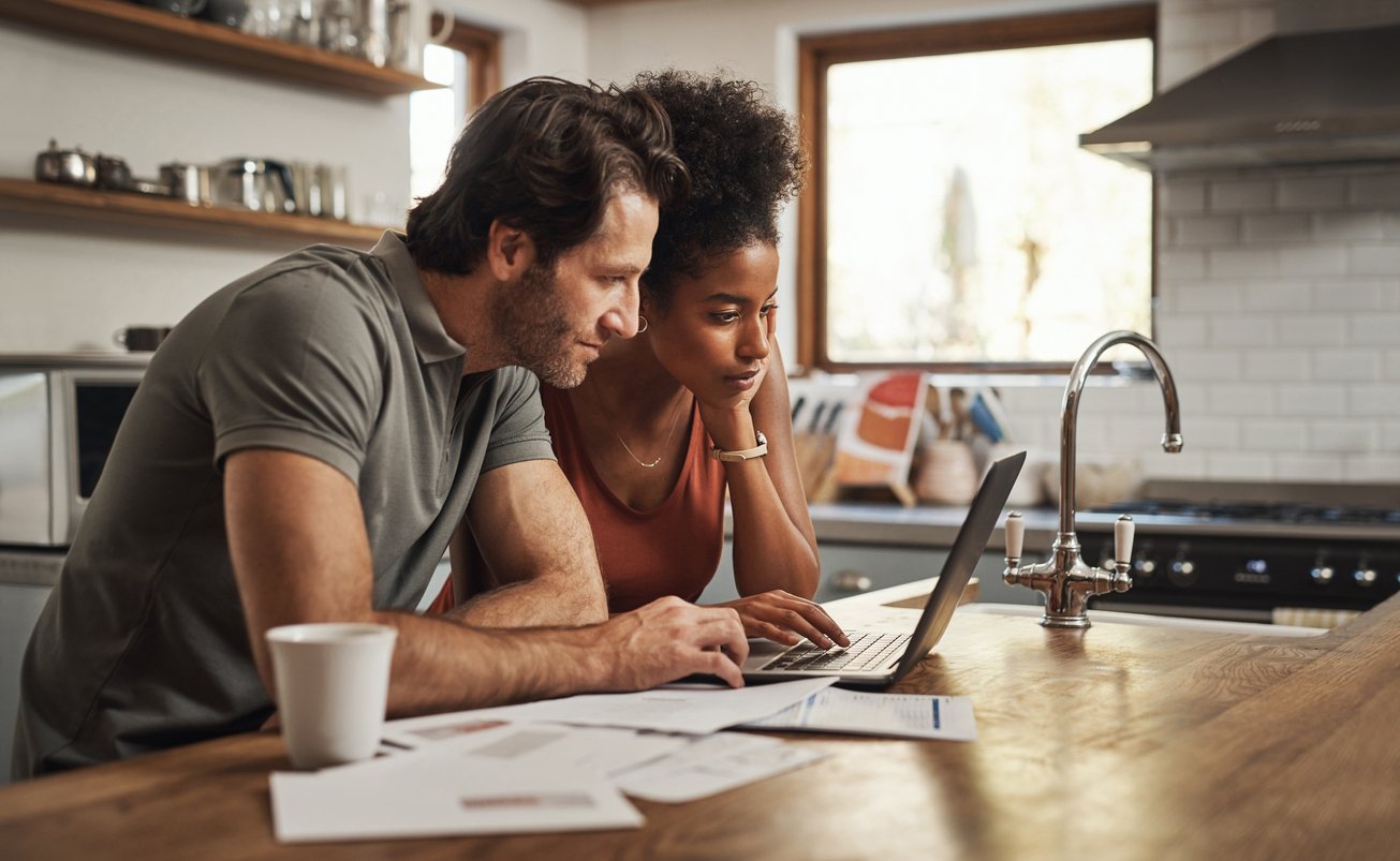 A young couple sits in kitchen doing taxes on a laptop.