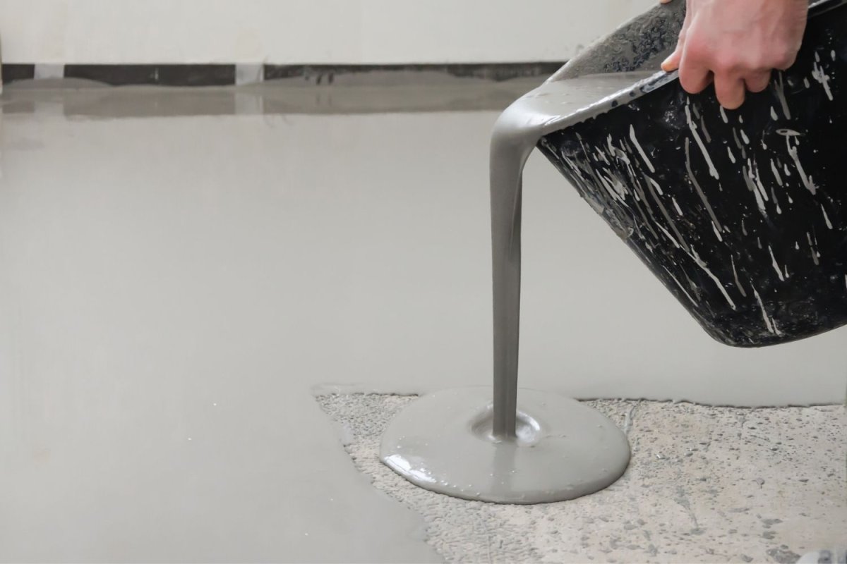 A black container of epoxy floor coating is being poured onto a garage floor.