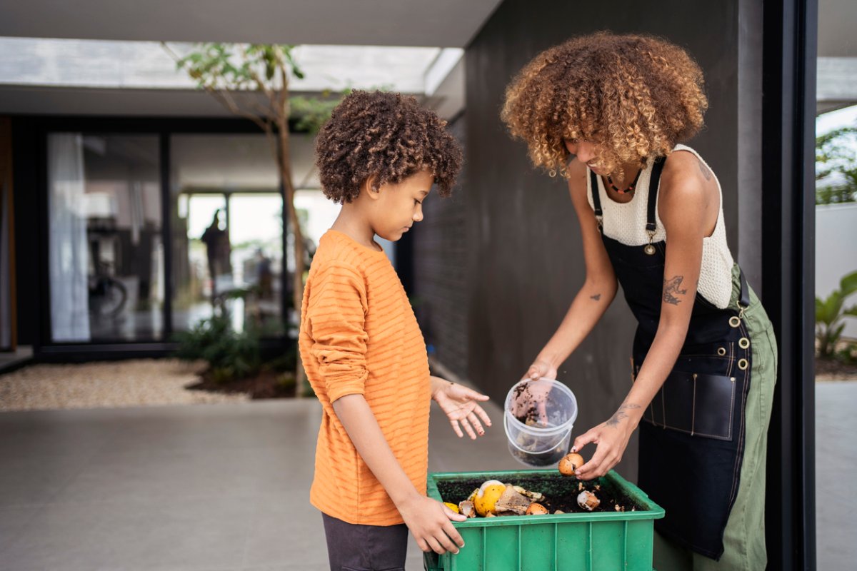 -parent-and-child-put-egg-shells-into-a-compost-bin-on-a-patio.