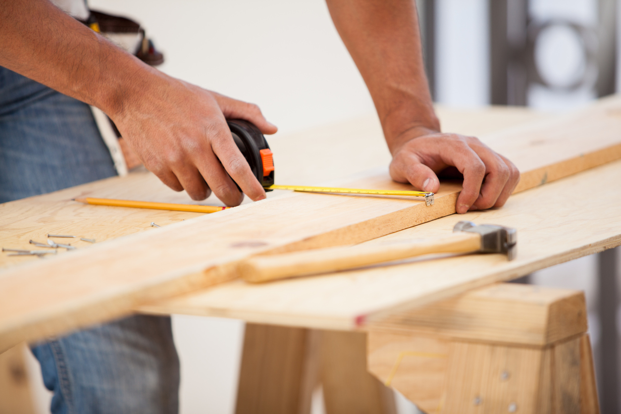 Closeup of a contractor usinga tape measure to mark down some dimensions on a wood board