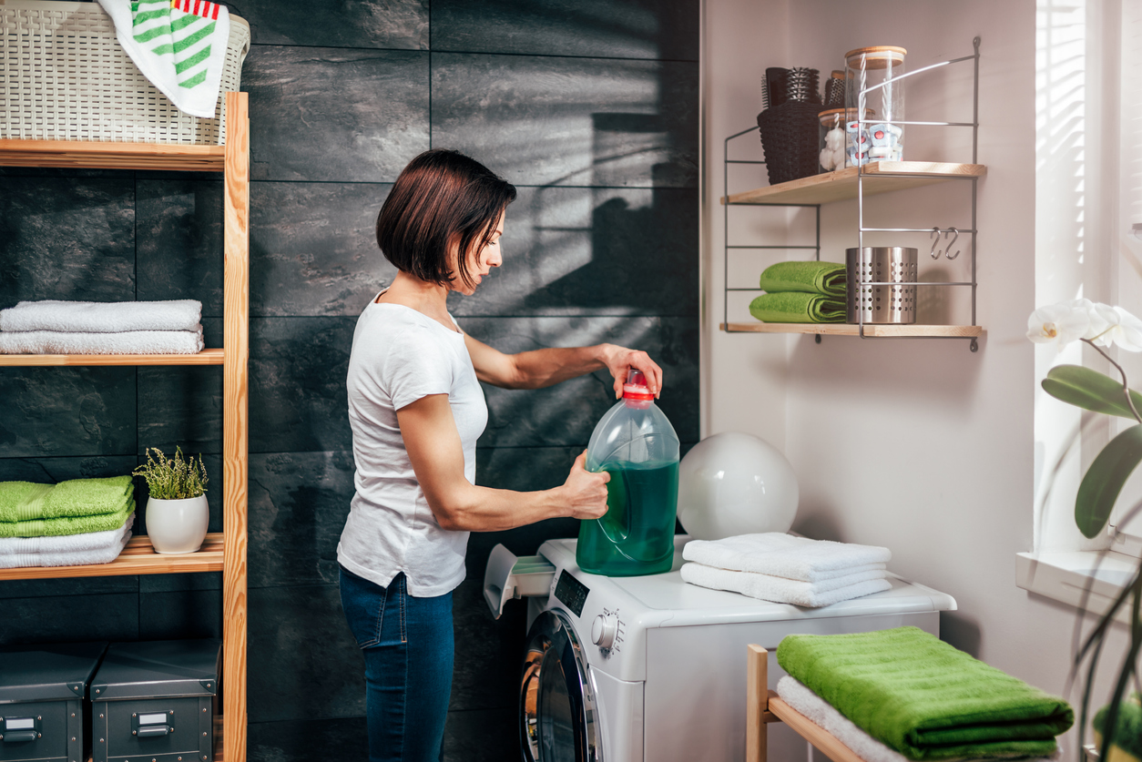 Women standing in front of washing machine and opening bottle of liquid detergent