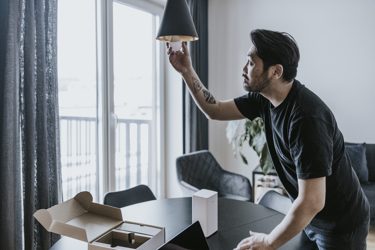 man with tattooed arm changing light bulb on ceiling fixture in small living room