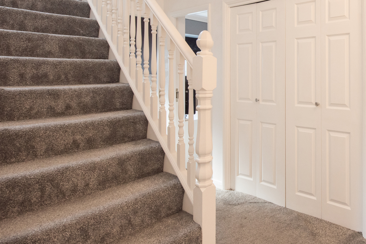 A grey waterfall style carpeted staircase leads into the hallway of a home.