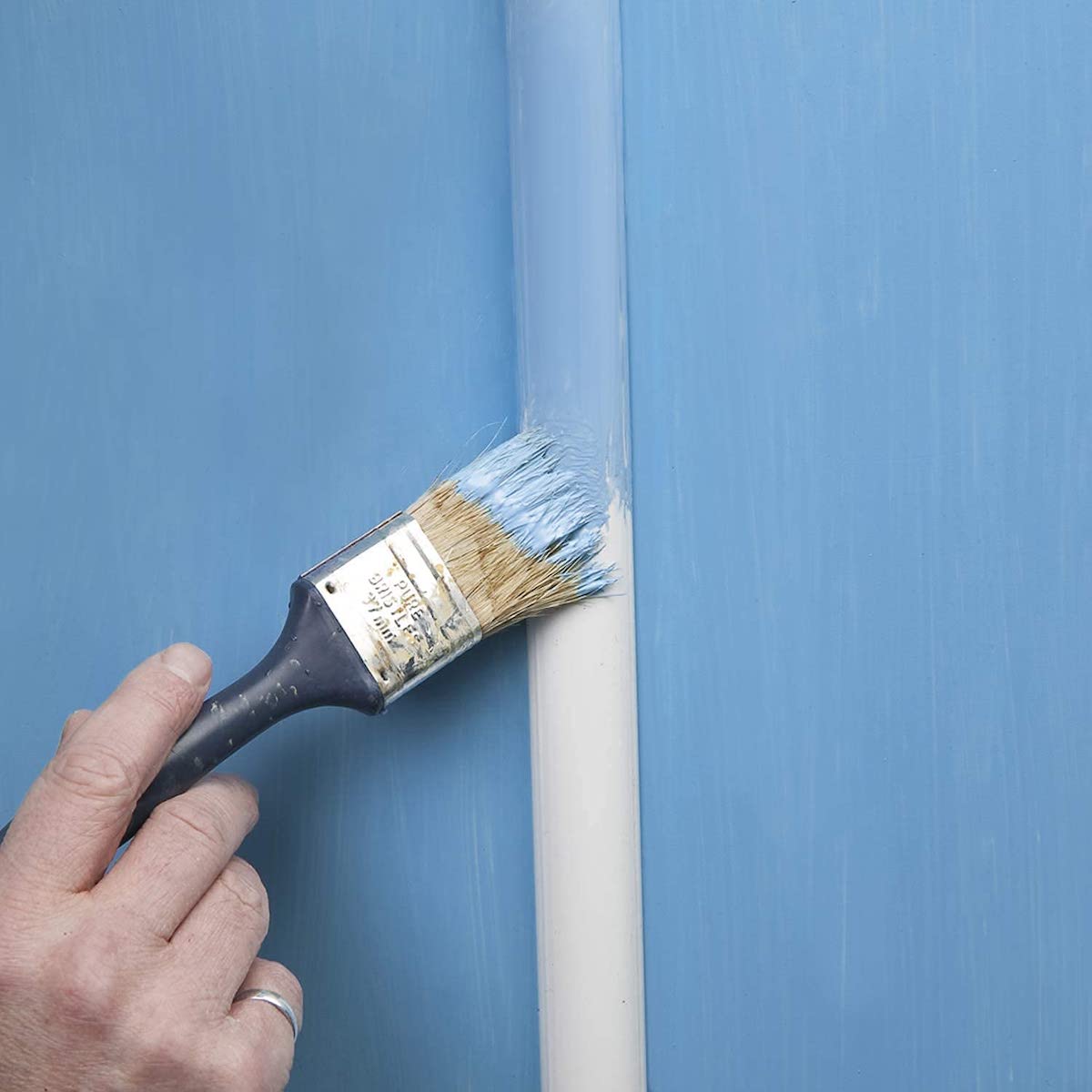 Une personne peint un chemin de câbles blanc en bleu clair pour l'assortir à la peinture murale bleu clair.