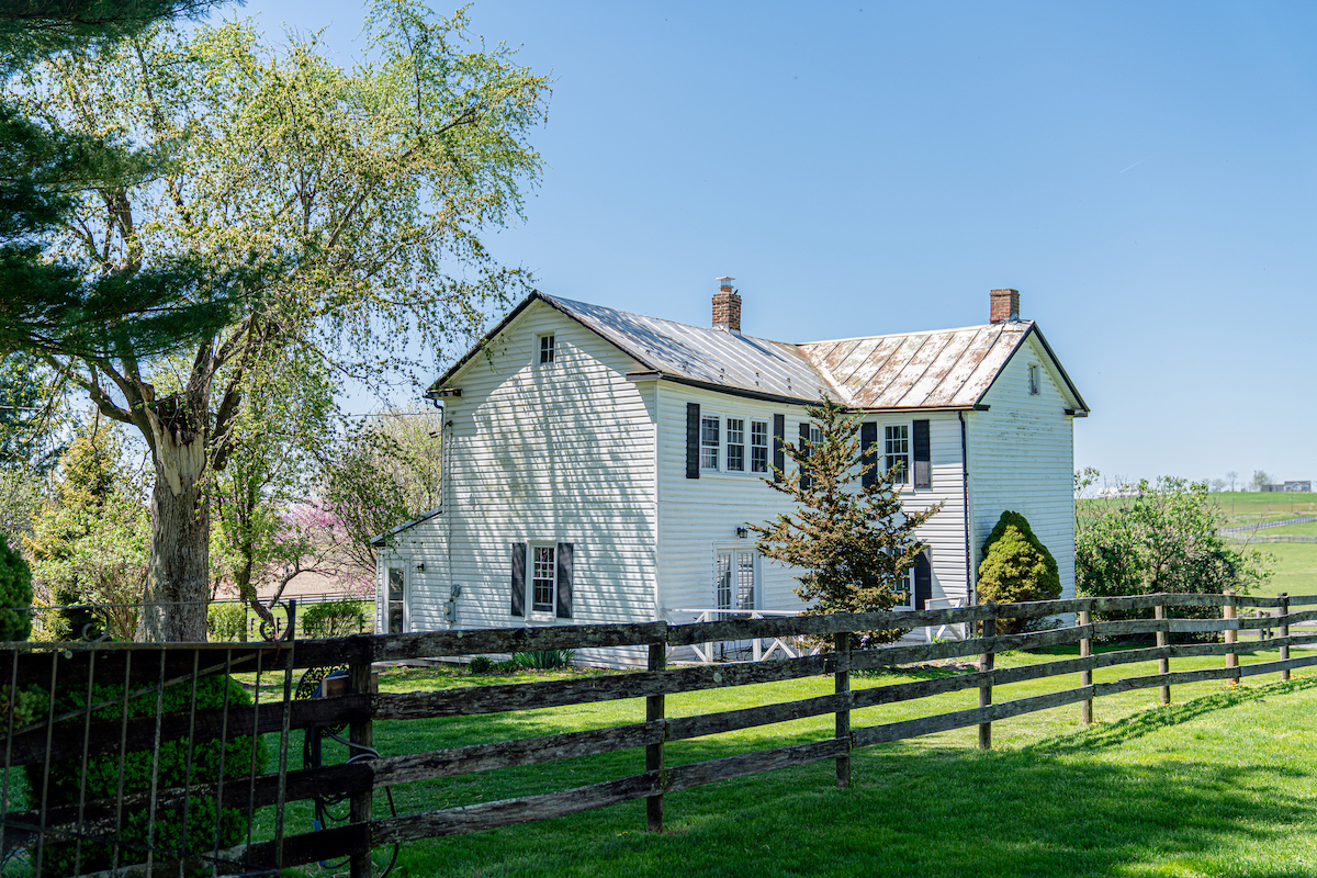 Une clôture en bois à claire-voie borde la cour d'une maison de ferme de style colonial.