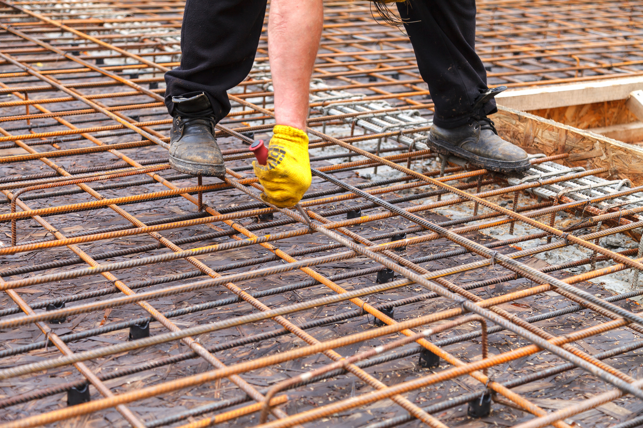 The worker ties steel reinforcing bars with wire to strengthen the foundation. Close-up. Daylight.