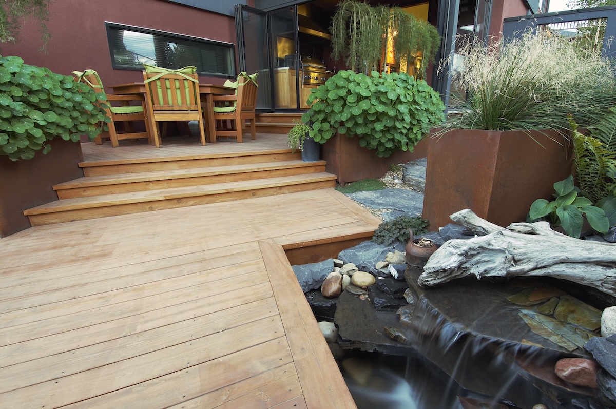 Une terrasse moderne avec des jardinières et un étang entouré de pierres. 