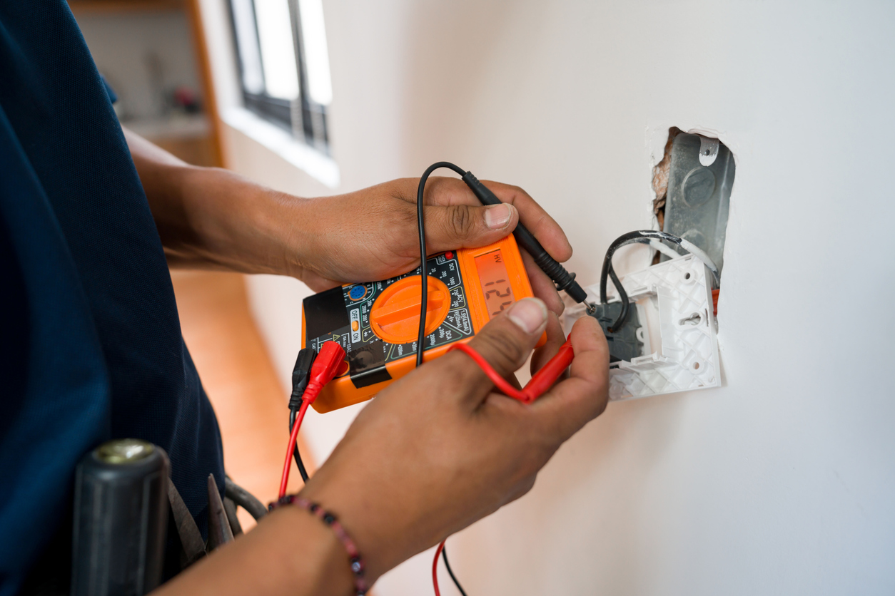 Électricien réparant une prise électrique et mesurant la tension