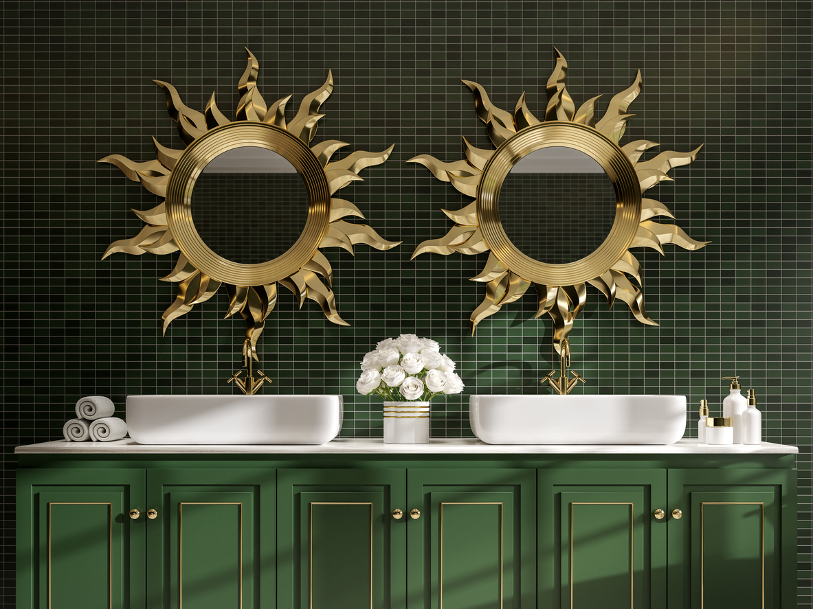 Une salle de bains avec des vitres et des carreaux muraux vert foncé est décorée d'accents en or et de miroirs à cadre en or en forme de soleil.