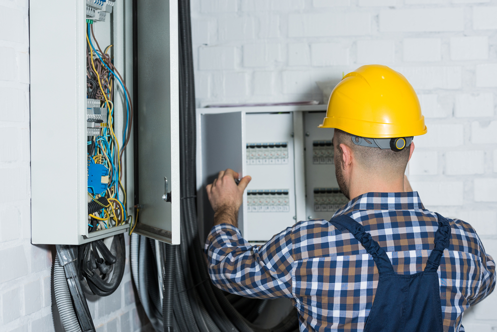 A worker in a yellow hard hat assesses an electrical panel.