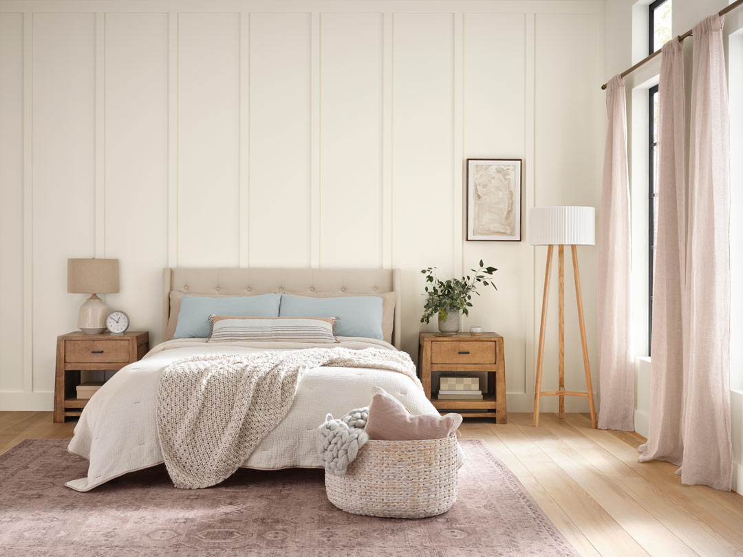 Bedroom with beige bedding and light wood floors with walls painted in Alabaster by Sherwin-Williams.