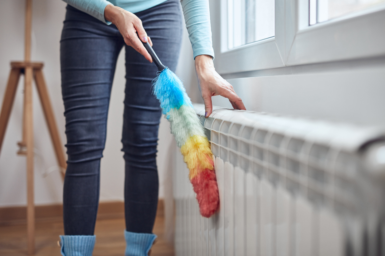 Femme avec un bâton à poussière nettoyant le radiateur à gaz du chauffage central à la maison