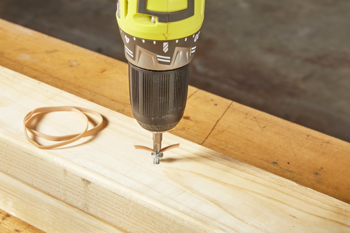 A person using a rubber band to remove a stripped screw embedded in a wood stud.