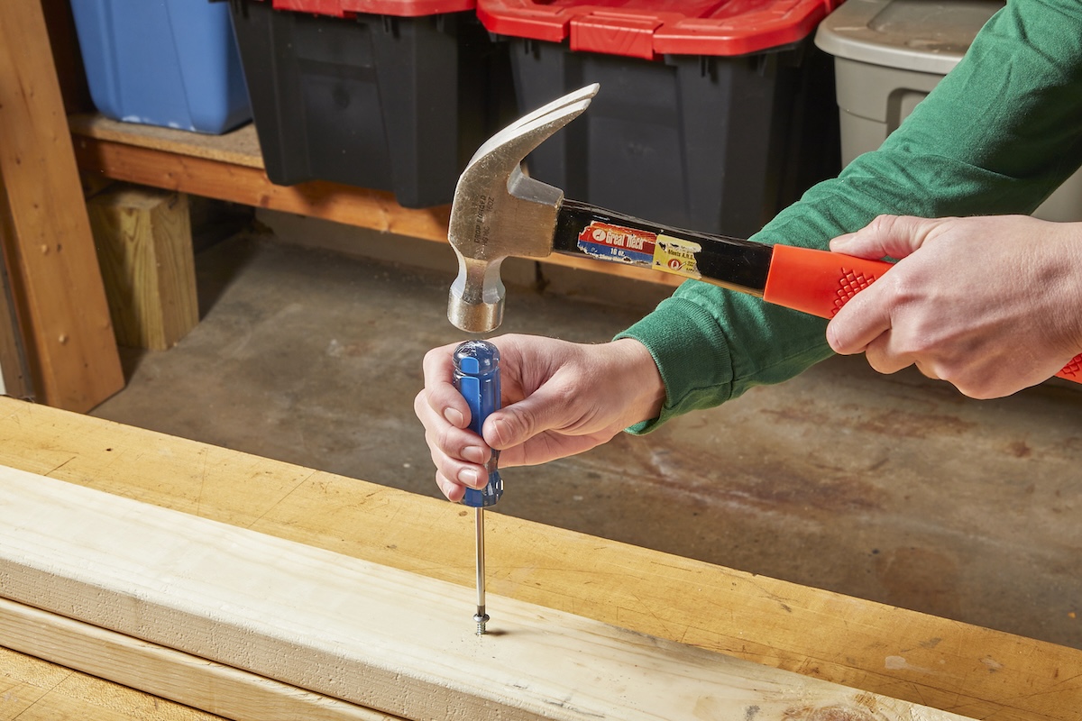 A person using a hammer and a handheld screwdriver to remove a stripped screw.