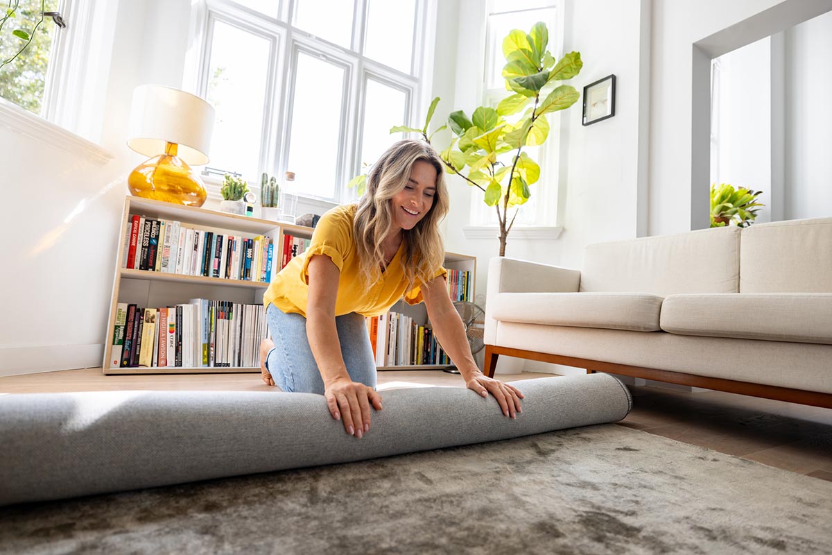 A woman rolls out a rug in a living room.